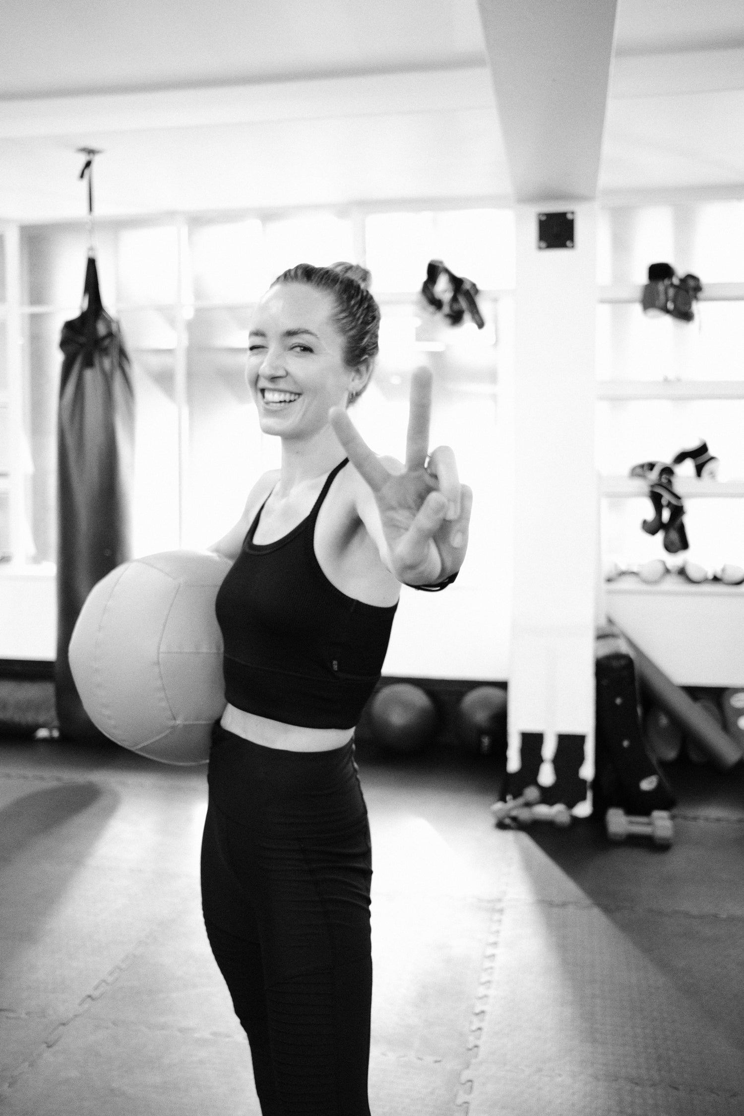 Coach Cords (Daniella Corder) - holding a medicine ball and showing the peace sign with her fingers.