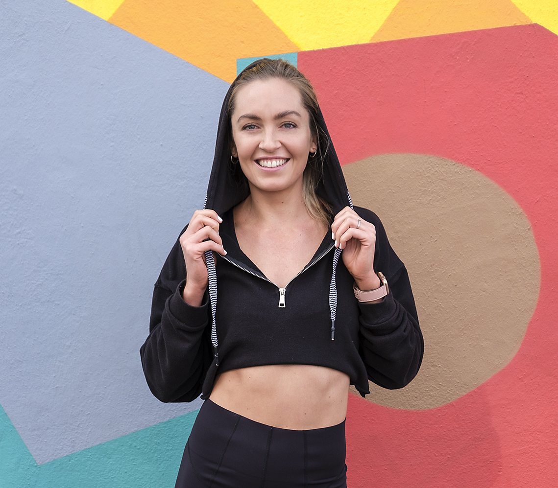 Coach Cords (Daniella Corder) - standing in front of a funky wall design wearing active wear.